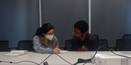 Two people seated at a desk, looking at notes.