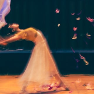 A slightly out of focus woman dancing in profile, with her back arched and arms stretched behind her, Leaves falling next to her.