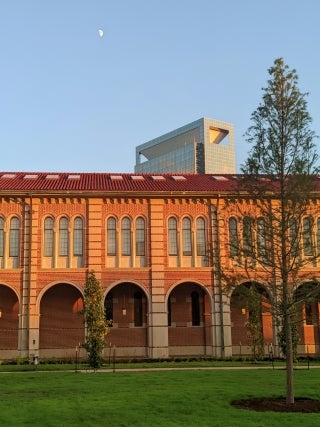 Part of a campus building with a medical center tower visible in the background and tree in front.
