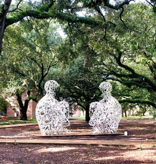 Art piece Mirror, two figures sitting facing each other, surrounded by trees.