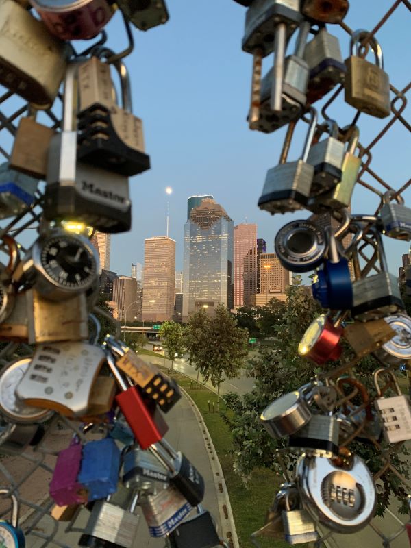 Houston skyline visible through a hole in a fence containing several locks