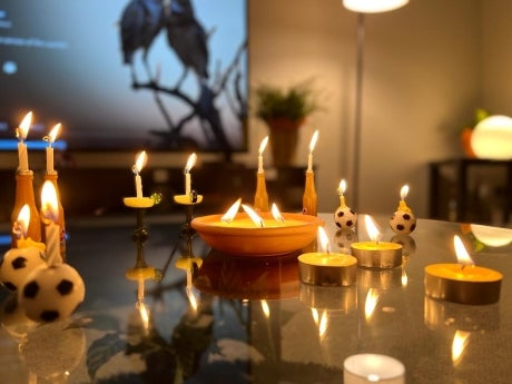 Several various lit candles on a table. Flames are reflected on the surface of the table.