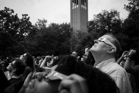Black and white image of a group of people looking up towards the sky, wearing eclipse glasses.