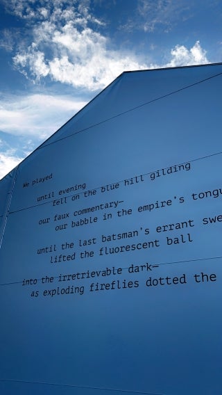 Side of the building with cloudy sky in the background. A partial poem is written on the wall.