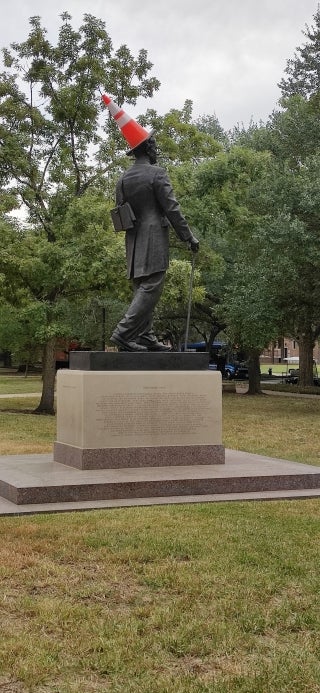 Statue of a person with an orange traffic cone on its head.