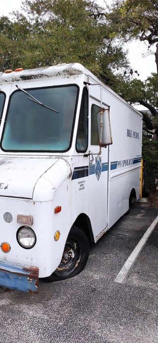 Front corner of an old, broken down white van. Rice Police markings are visible on the side of the vehicle.