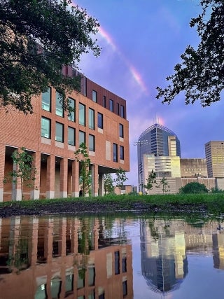 Buildings with their reflection in some water on the foreground. There is a rainbow in the sky behind them.