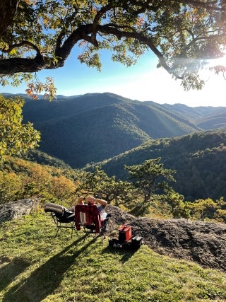Beautiful hilly landscape. A person seated in a lawn chair in the foreground, looking at the view.