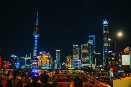 Lit up city skyline in the dark. People taking photos of it in the foreground.