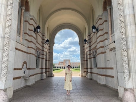 A woman stands facing the camera in the Sallyport archway of Lovett Hall. Fondren Library is visible in the background.