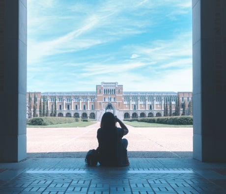 Person sitting at the foreground, facing the Rice University academic quad with Lovett Hall in the background.