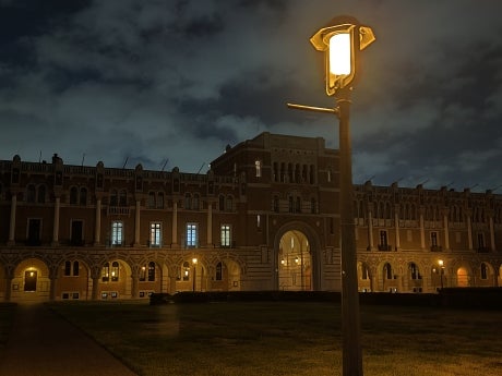 Lovett Hall at night. Lights are on outside the building. Foreground has a lamppost with the light on.