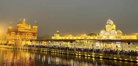 City view with ornate, bright light buildings. Water on the foreground with a lot of people sitting on the edge of the water.