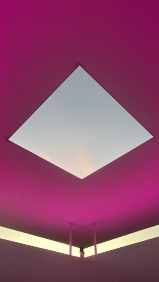 Light blue sky seen through the Skyspace. Pink light reflected to the ceiling around the window.