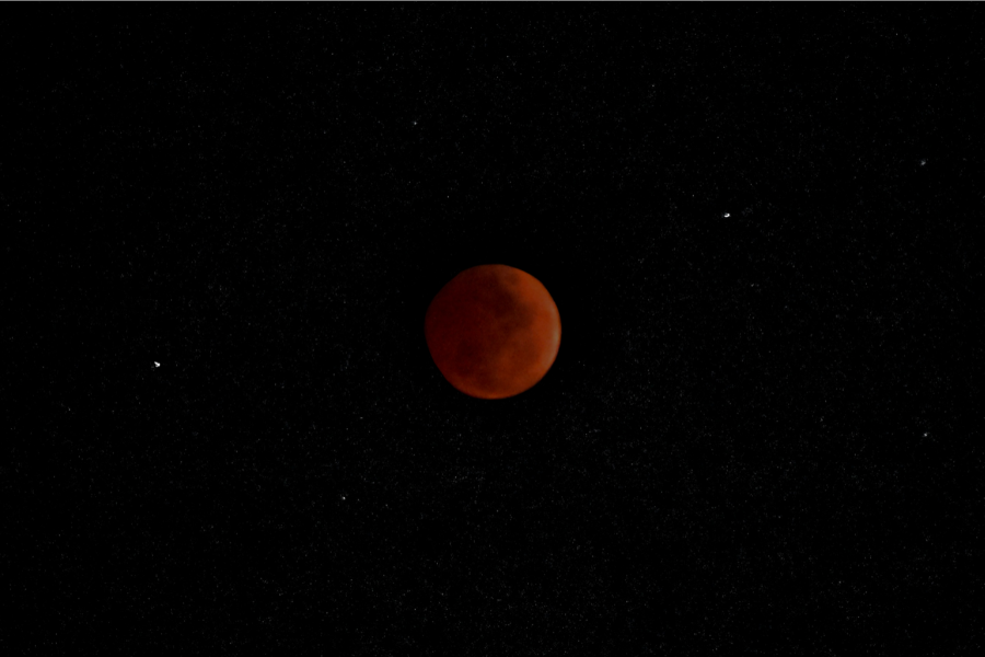 Lunar eclipse. Moon visible as a red circle in the middle of the image. Background is otherwise blank, but a few stars are visible.