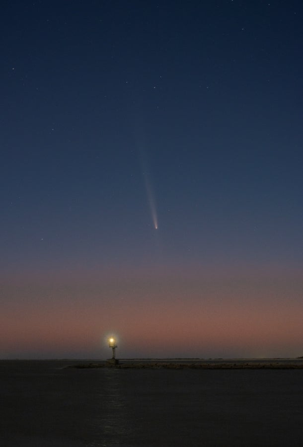 View of dark night sky at dush. A comet can be seen in the middle of the image, its tail clearly visible.